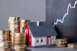House with stacks of money and a rising curve symbolizing rising real estate prices