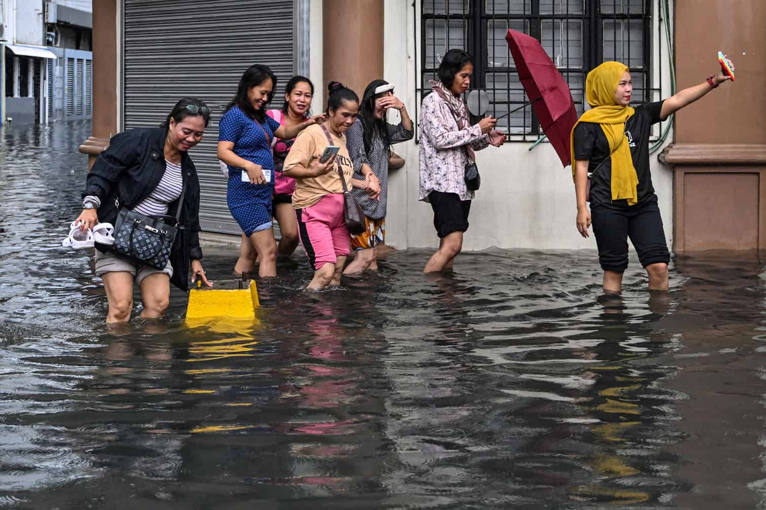 A woman poses for a selfie while wading with others through a flooded street