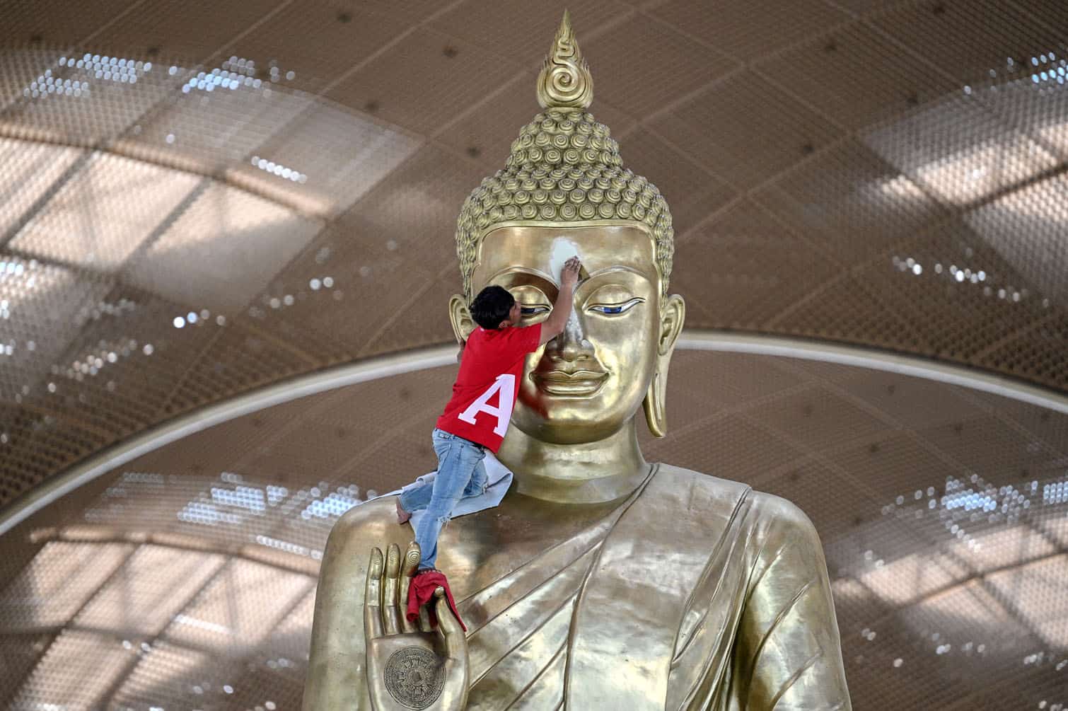 A worker cleans a statue of Buddha