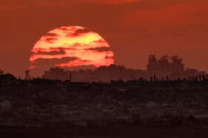 the sun sets behind destroyed buildings