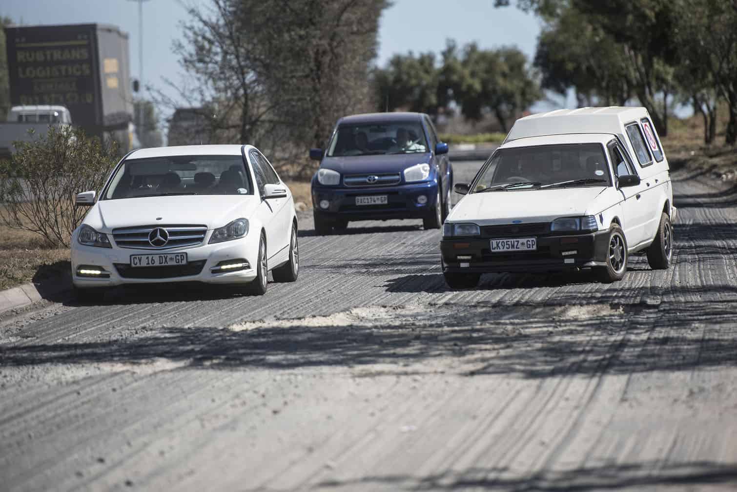 Vehicles travel along South Rand Road dodging road damage