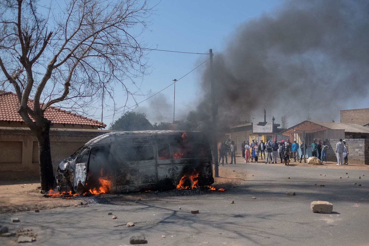 Residents look at a minibus taxi that was set alight