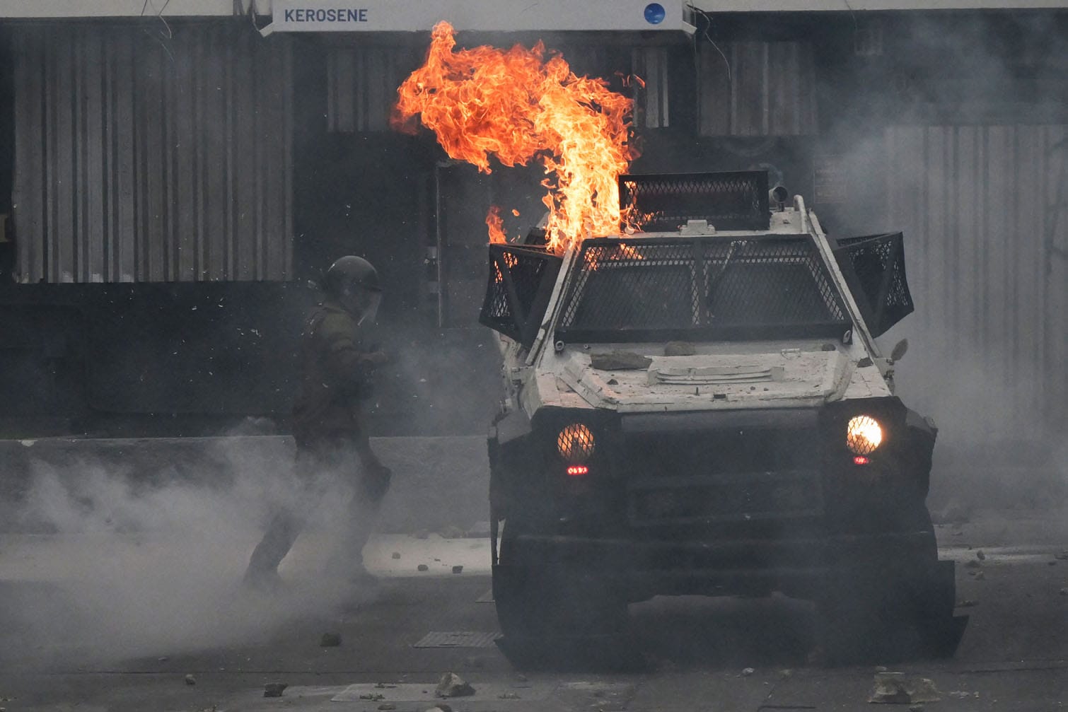 A riot policeman stands next to a vehicle set on fire