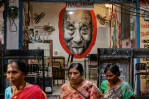 Local women walk past a portrait of the Tibetan spiritual leader Dalai Lama