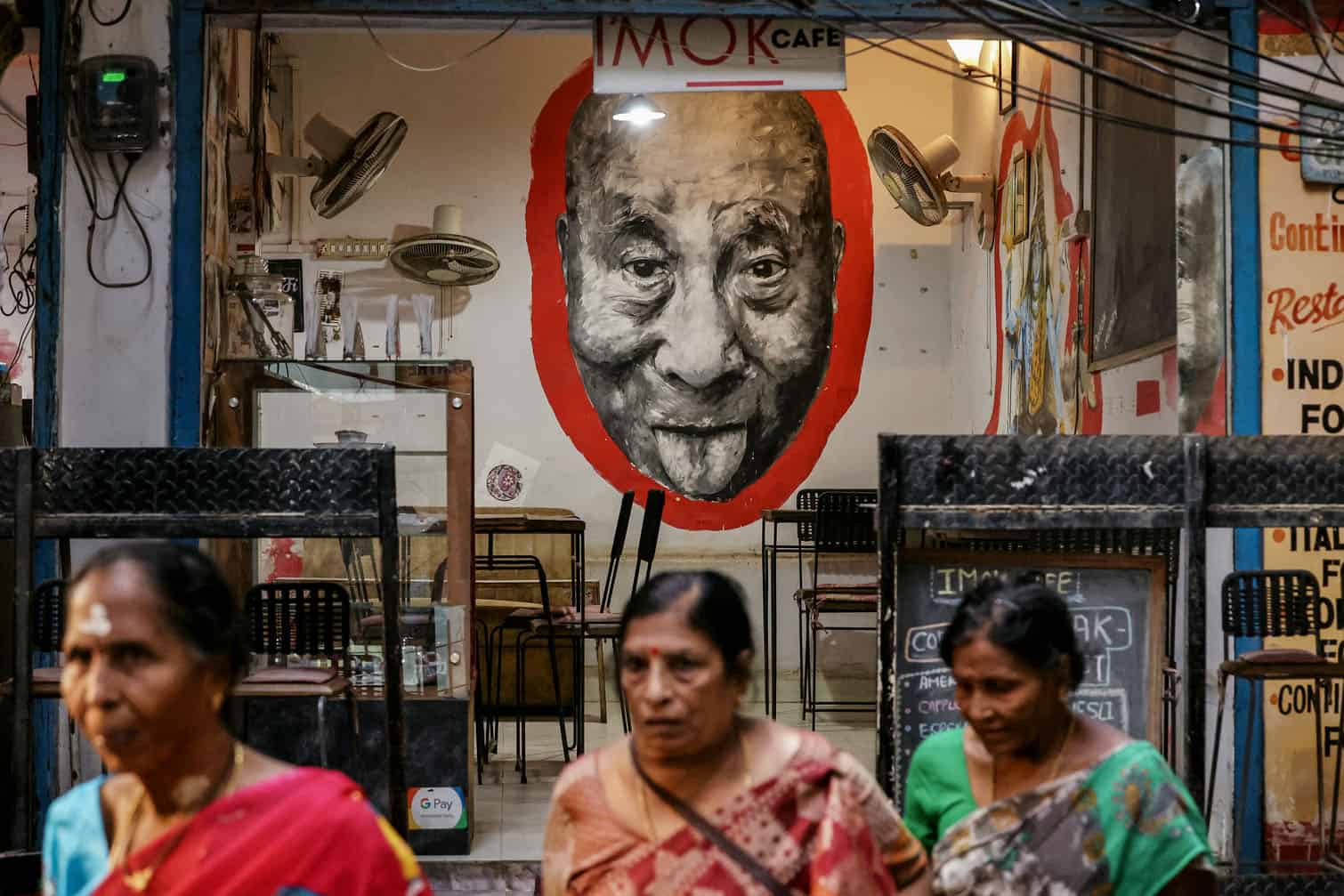 Local women walk past a portrait of the Tibetan spiritual leader Dalai Lama