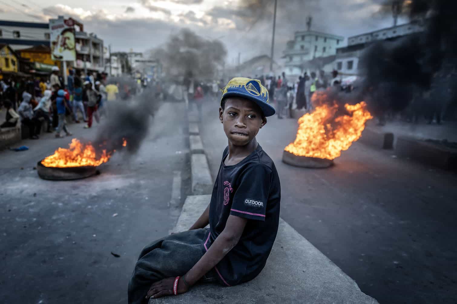 A boy sits atop a wall as he watches clashes between protesters and Malagasy security