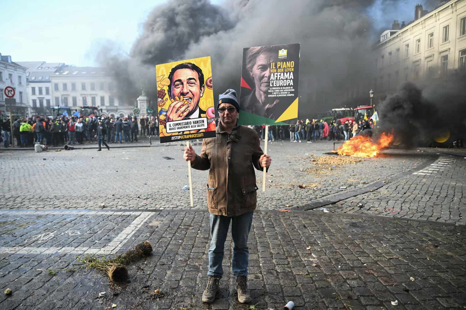 A farmer holds signs as farmers stand next to tractors