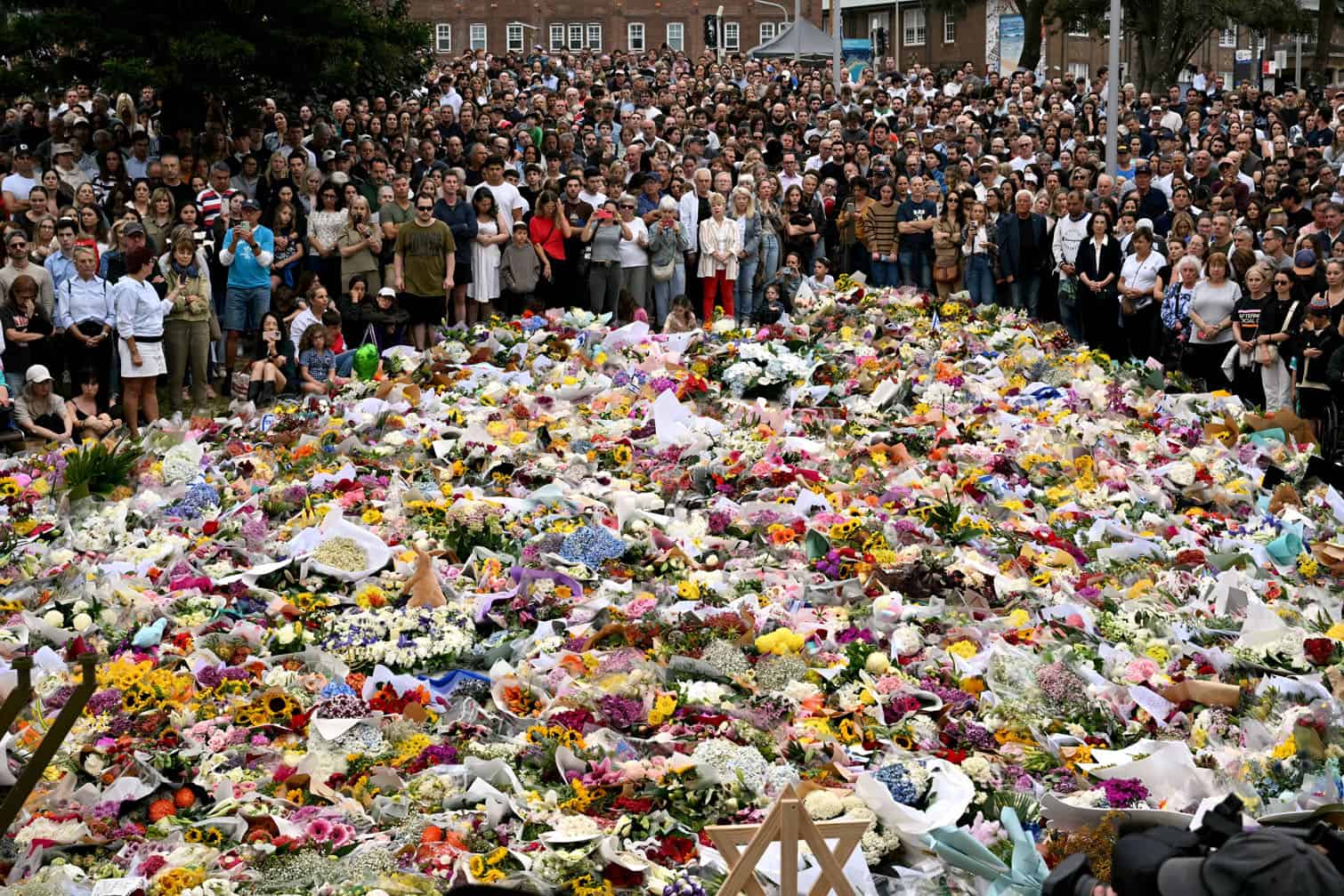 Mourners stand near tributes piled together