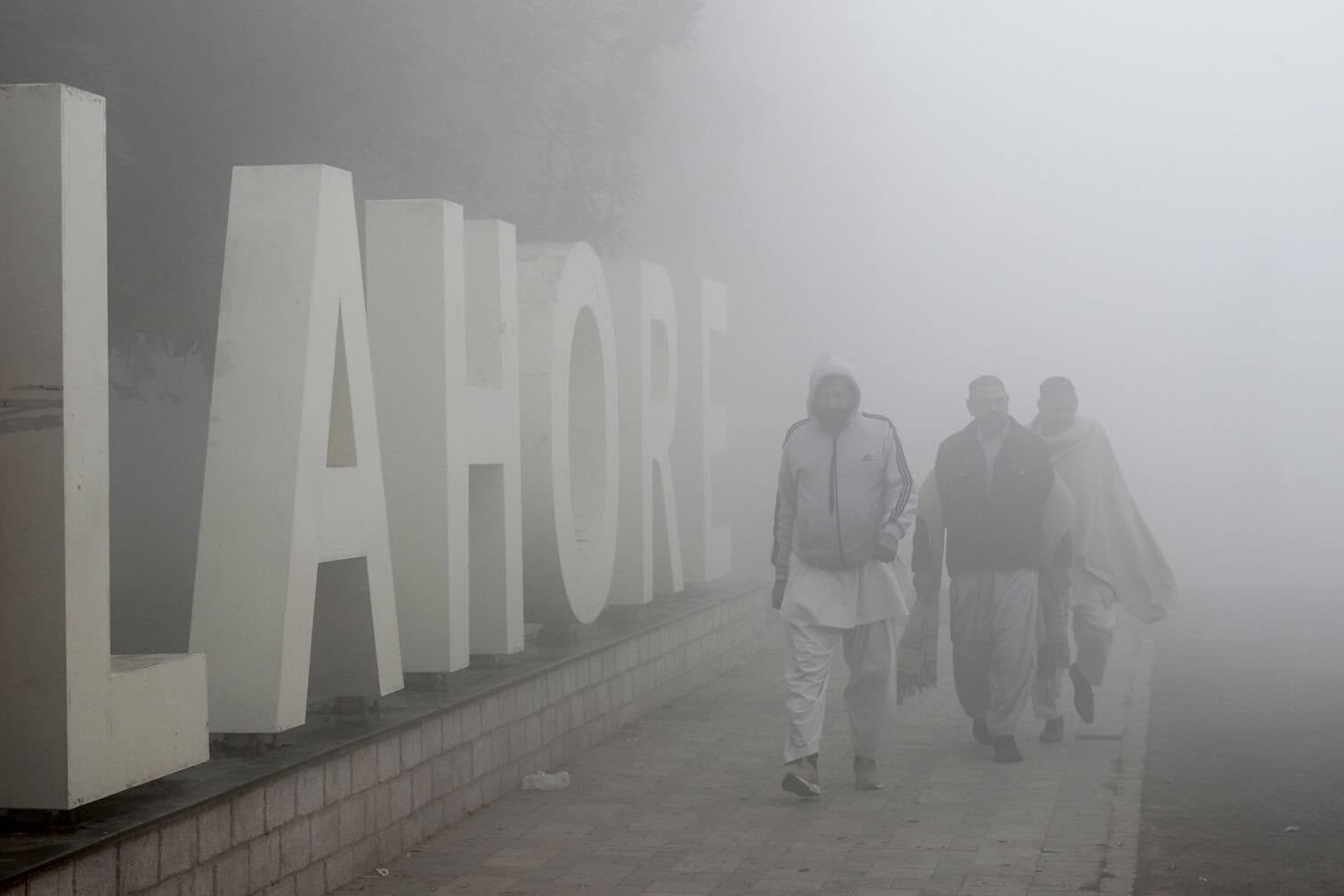 People walk across a park amid dense smog