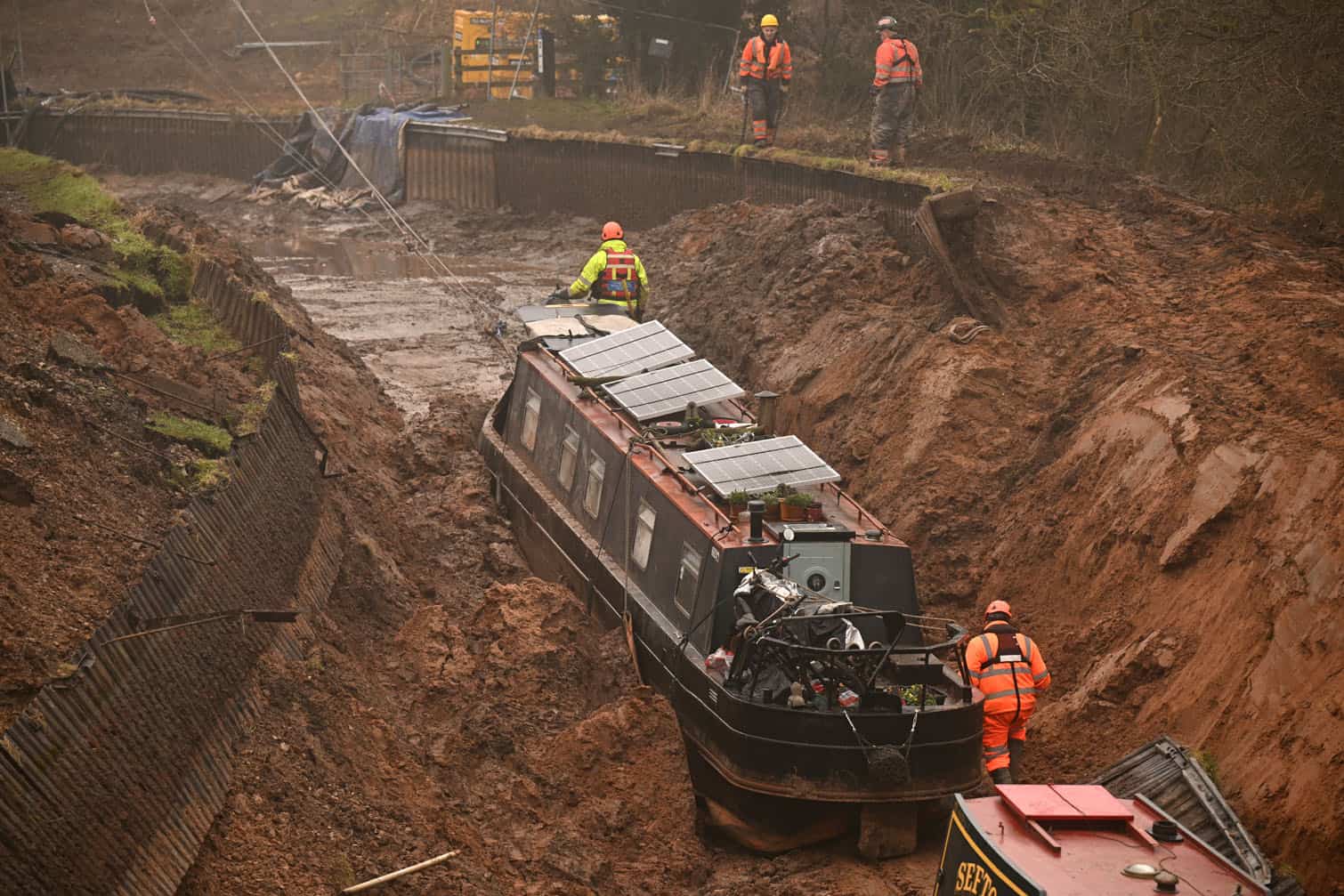 A stranded narrowboat is winched from in a collapsed canal