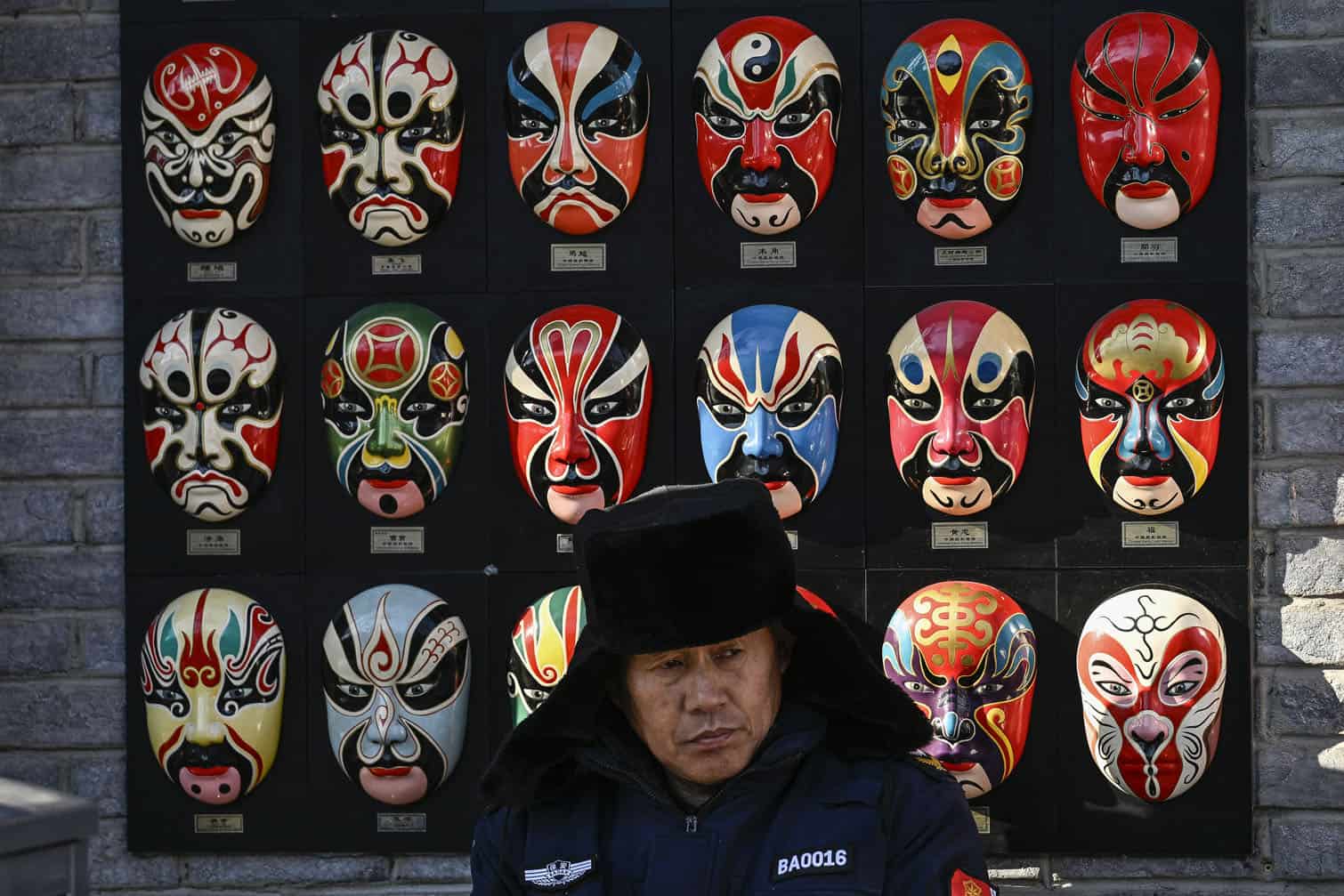 A security guard sits in front of a wall with traditional Chinese opera facemasks