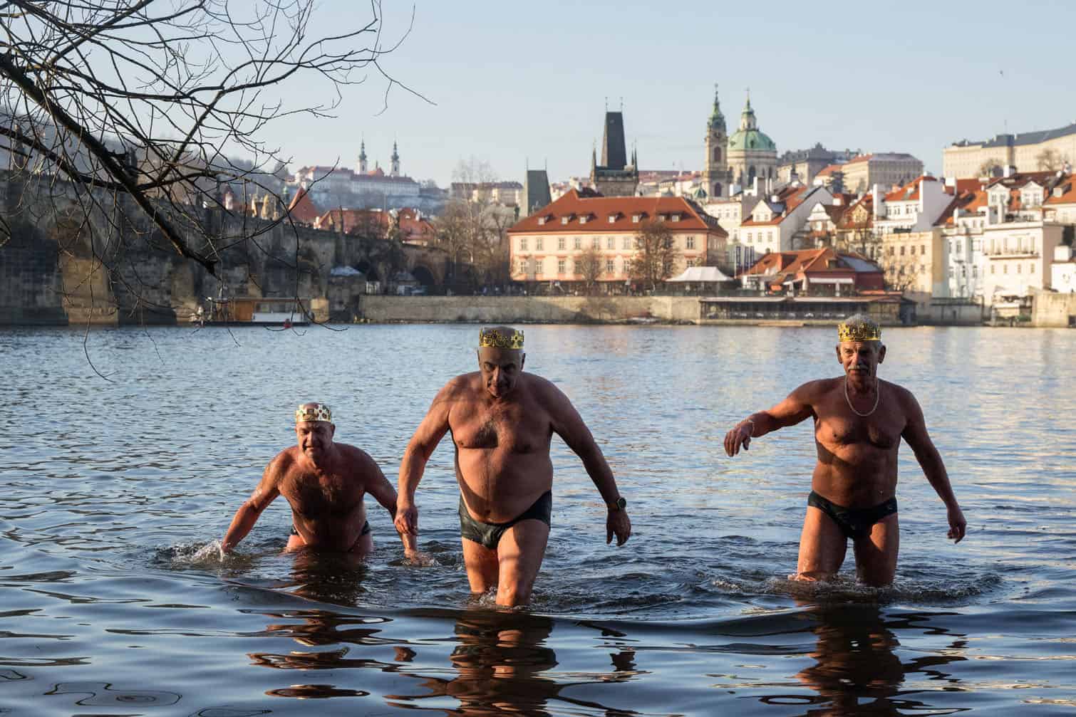 Wearing crowns, three winter swimmers walk out of the water