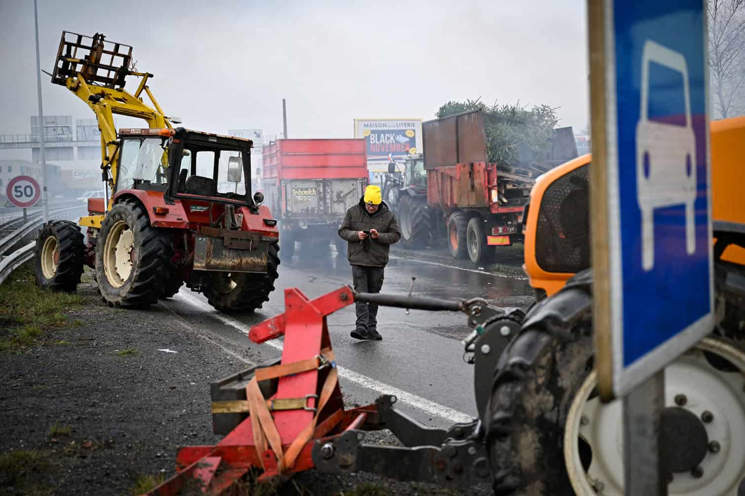 A protester looks at his phones as he walks among mechanical diggers