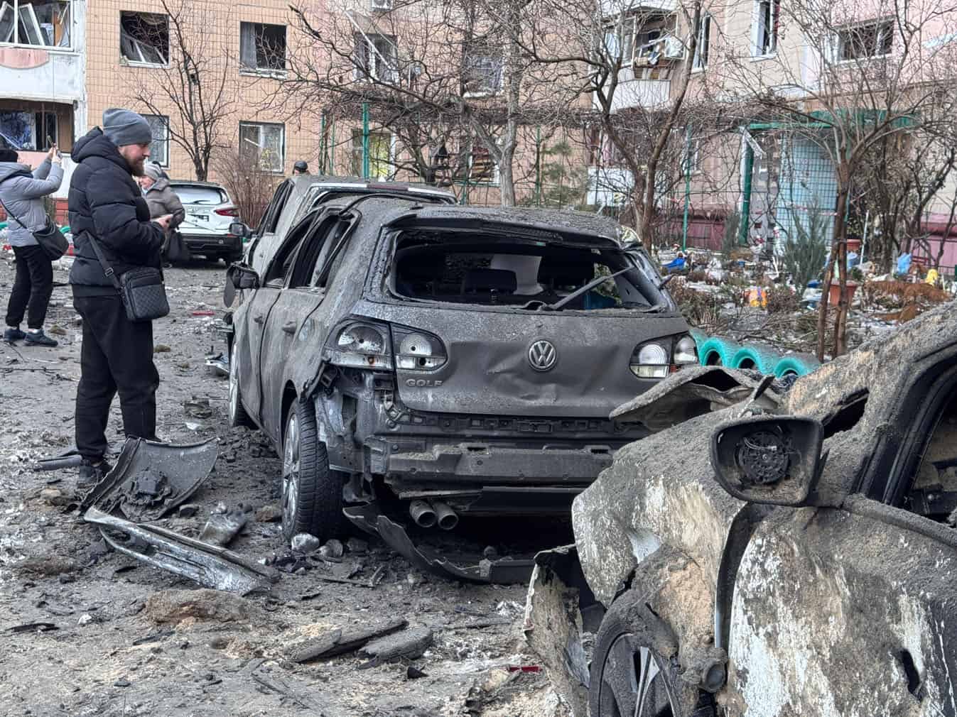 A man looks at a burned car in an area hit by an air attack