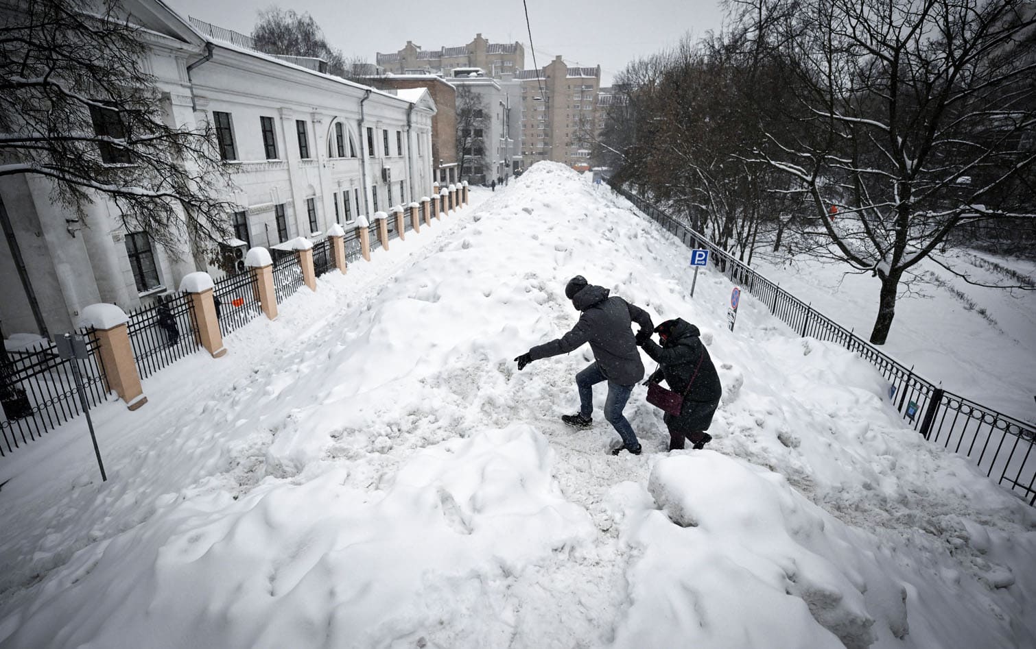People cross a street used for temporary snow storage