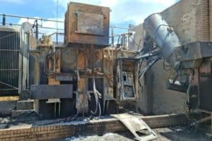 A damaged and burnt electrical substation transformer with charred components.