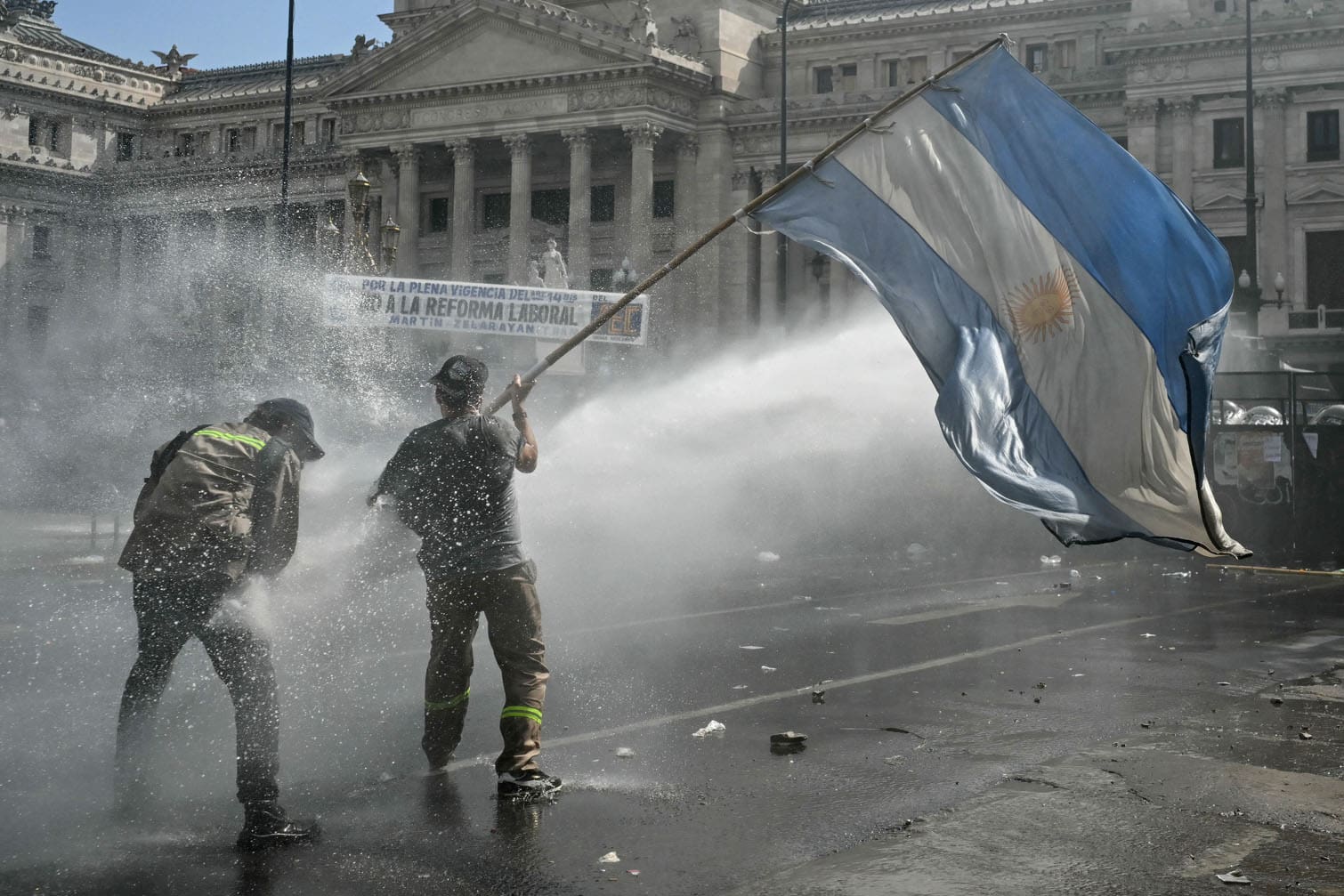 A demonstrator waving a national flag is hit by a water cannon