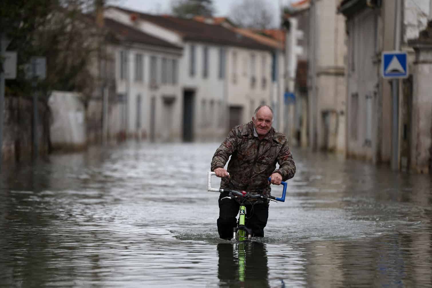 A man rides a bicycle through a flooded street