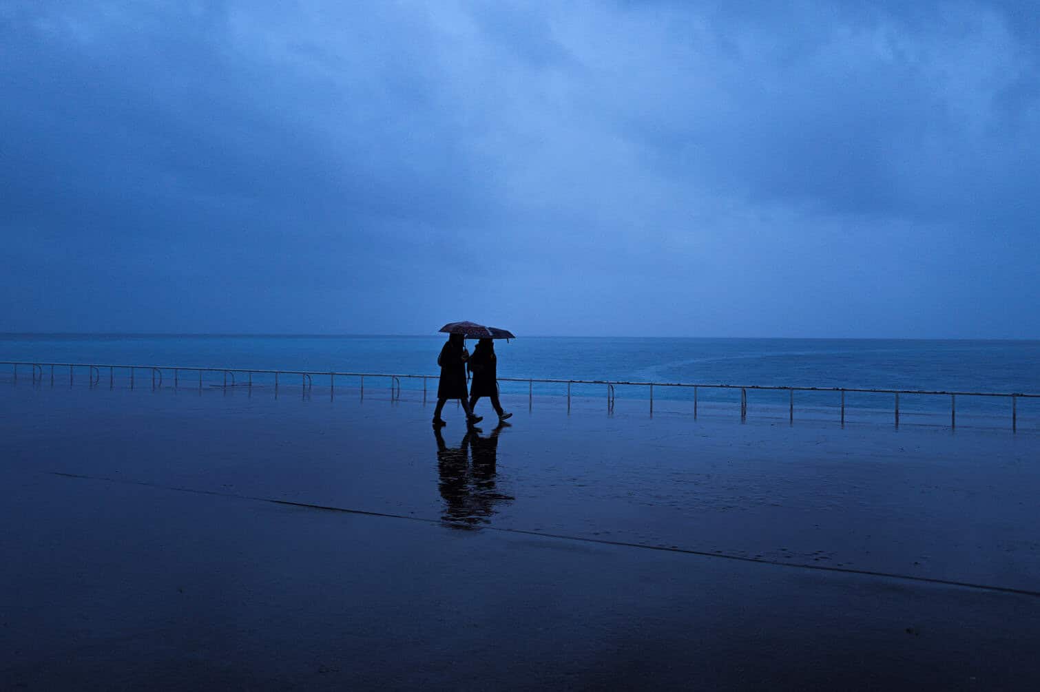 Two people walk in the rain holding their umbrella