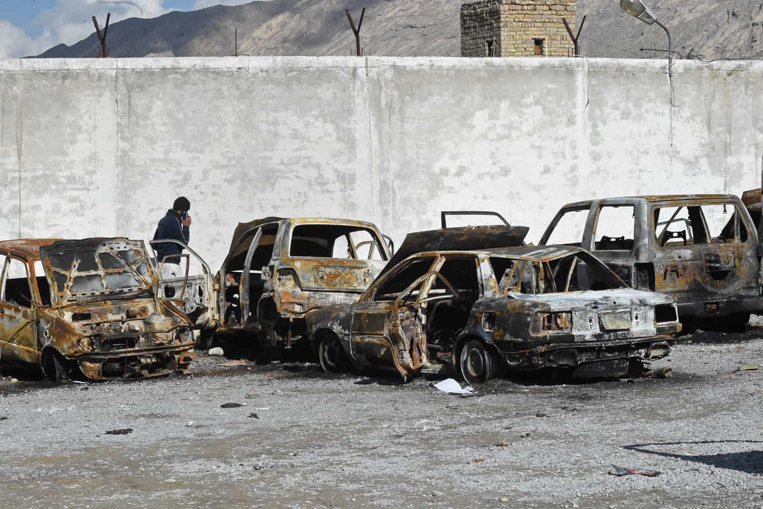 A man walks past burnt vehicles