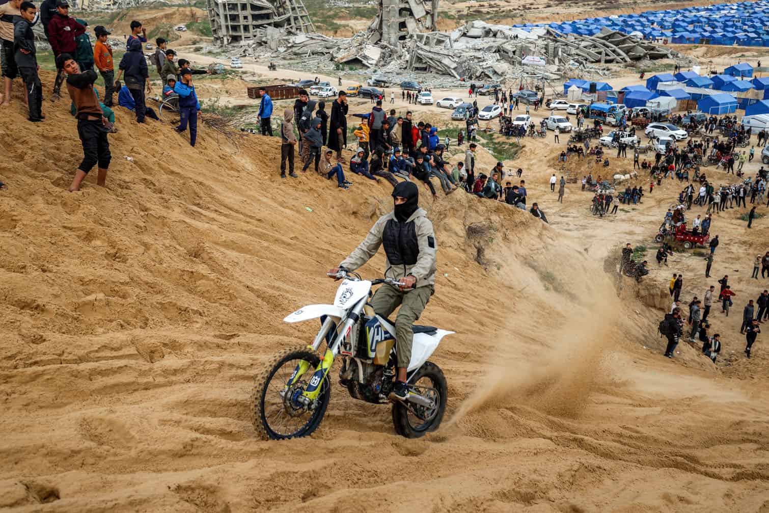 A man performs stunts with a dirt bike on sand dunes