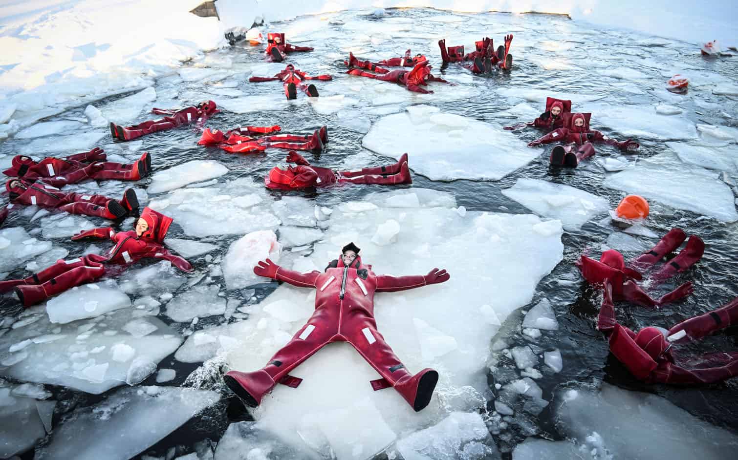 Participants wearing isothermal wetsuits float among ice floes