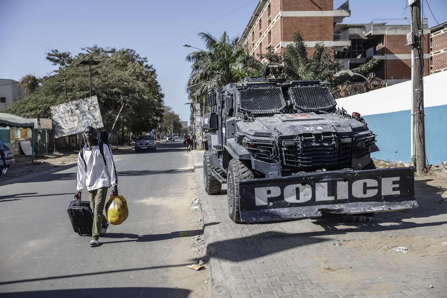 A student carries his belonging as he walks past as Senegalese police armored vehicle