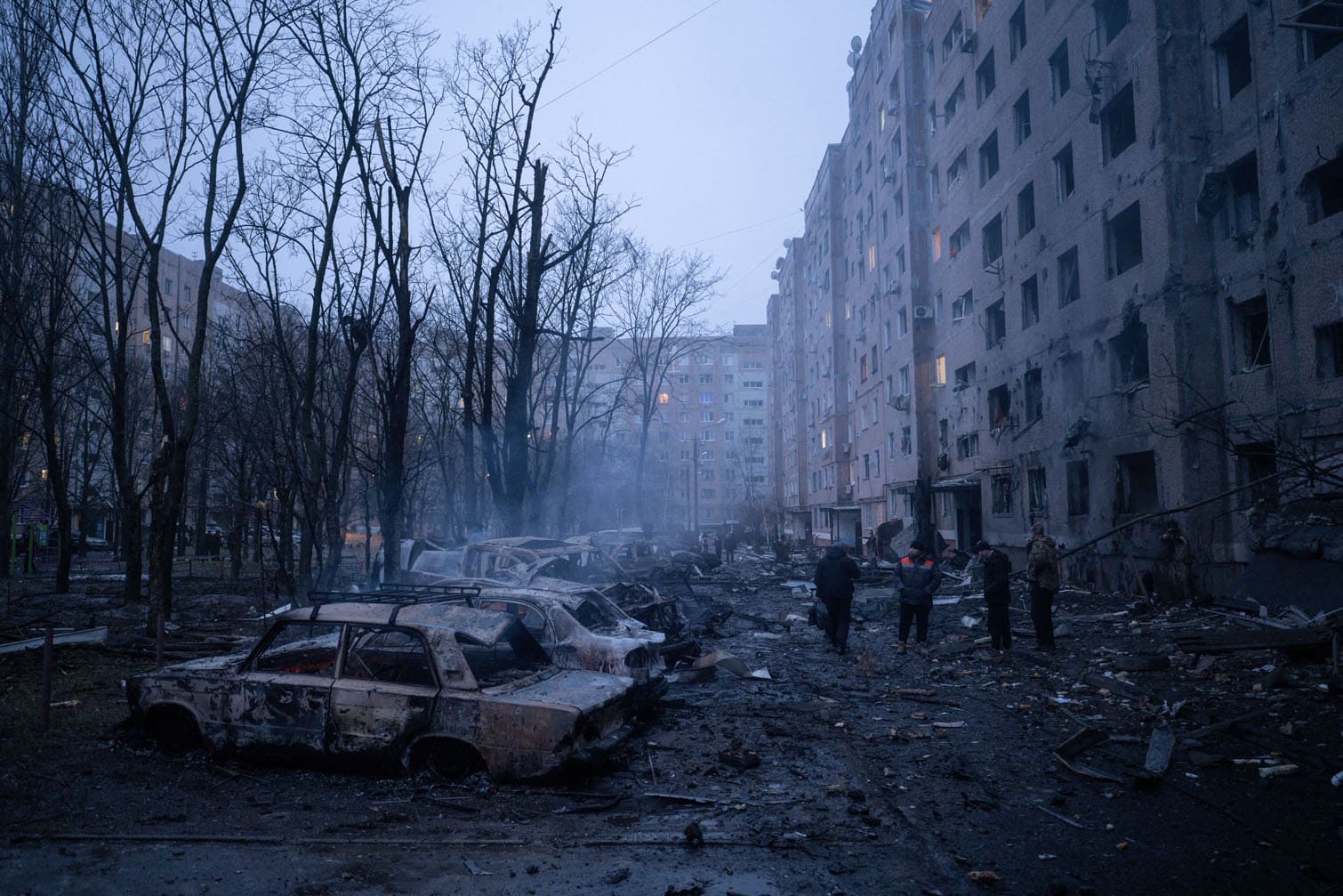 local residents stand next to burnt-out cars