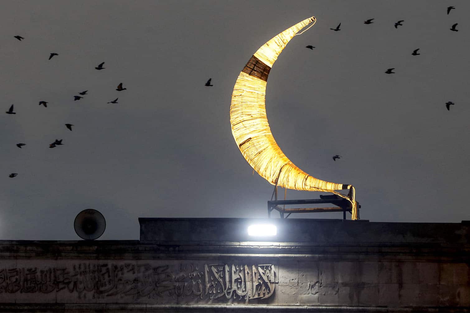 Birds fly past an installation depicting a crescent moon