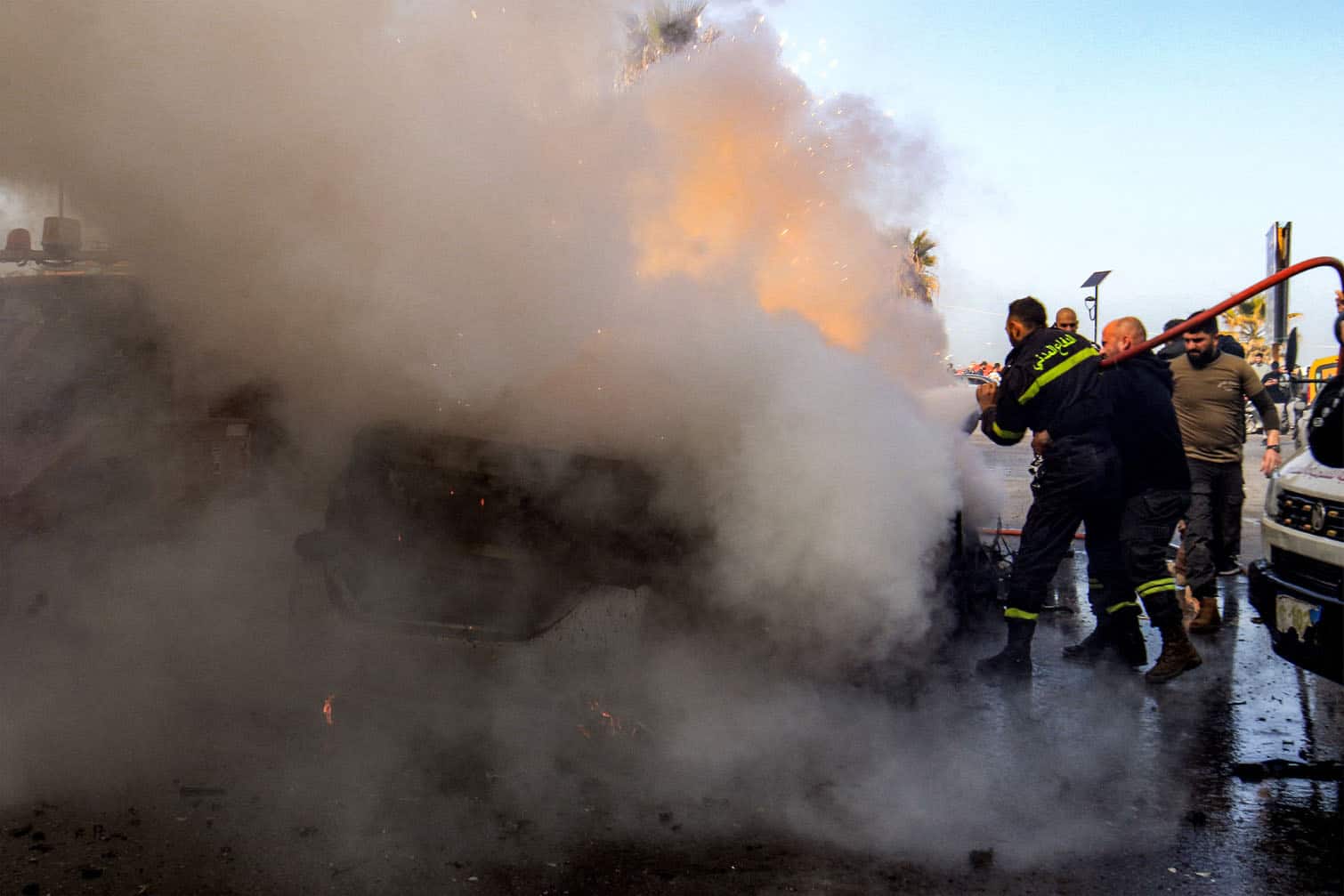 Firefighters extinguish a burning destroyed vehicle