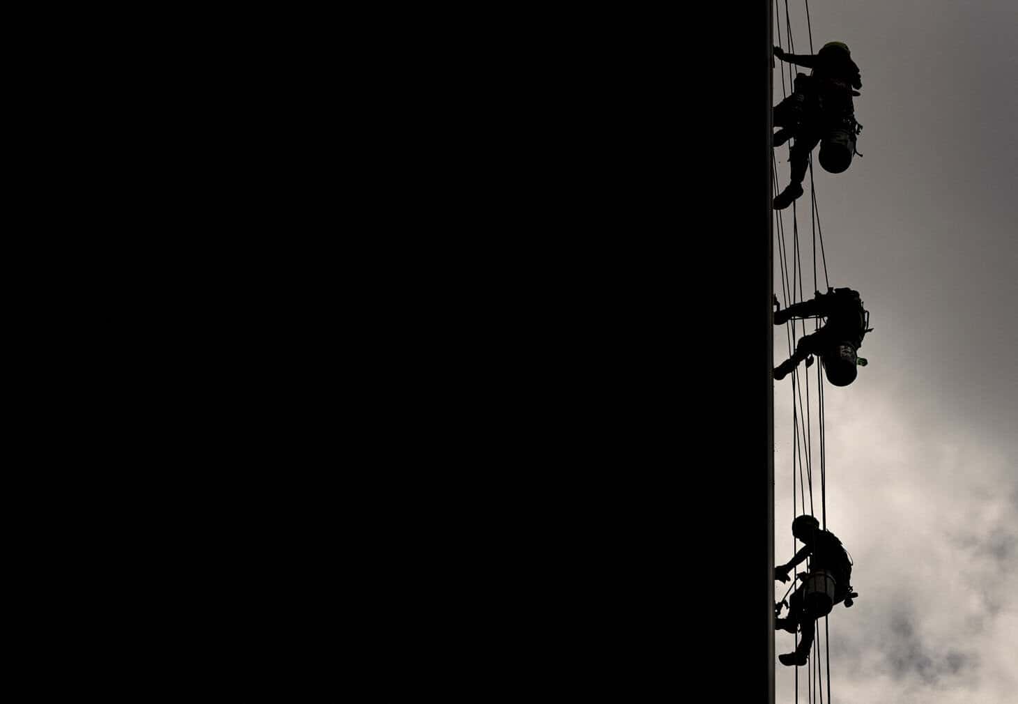 The silhouettes of three workers are seen cleaning the windows of a building