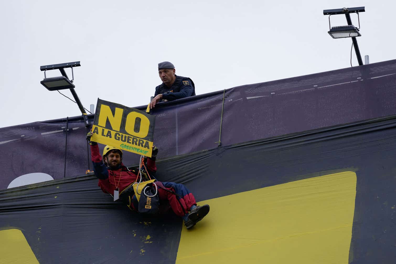 A police officer looks on as a Greepeace activists displays a placard
