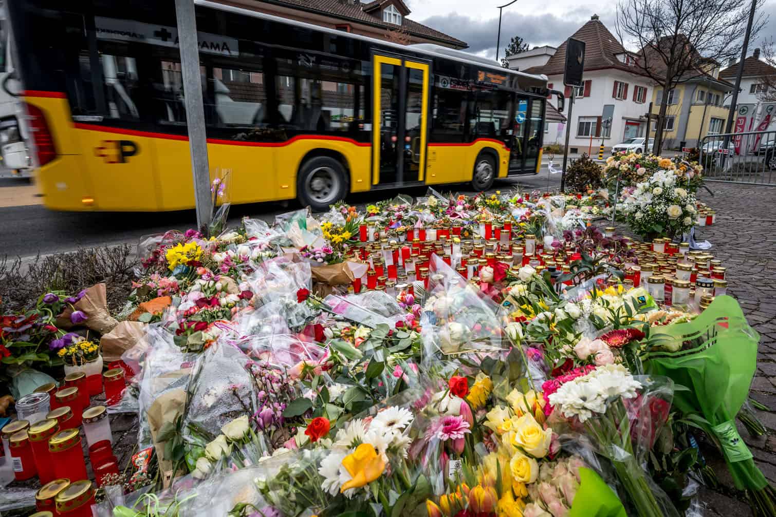 A PostBus passes flowers and candles