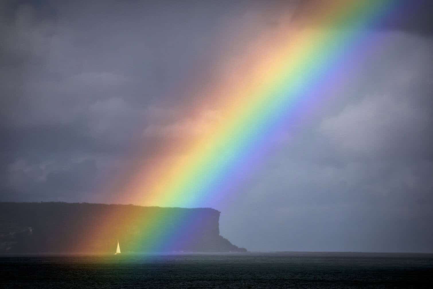 A sailing boat passes a rainbow