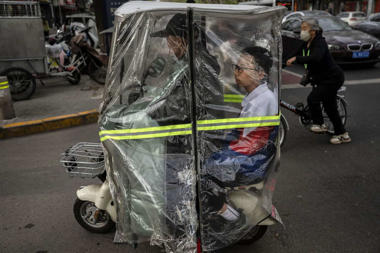 A student rides on the back of a covered electric scooter