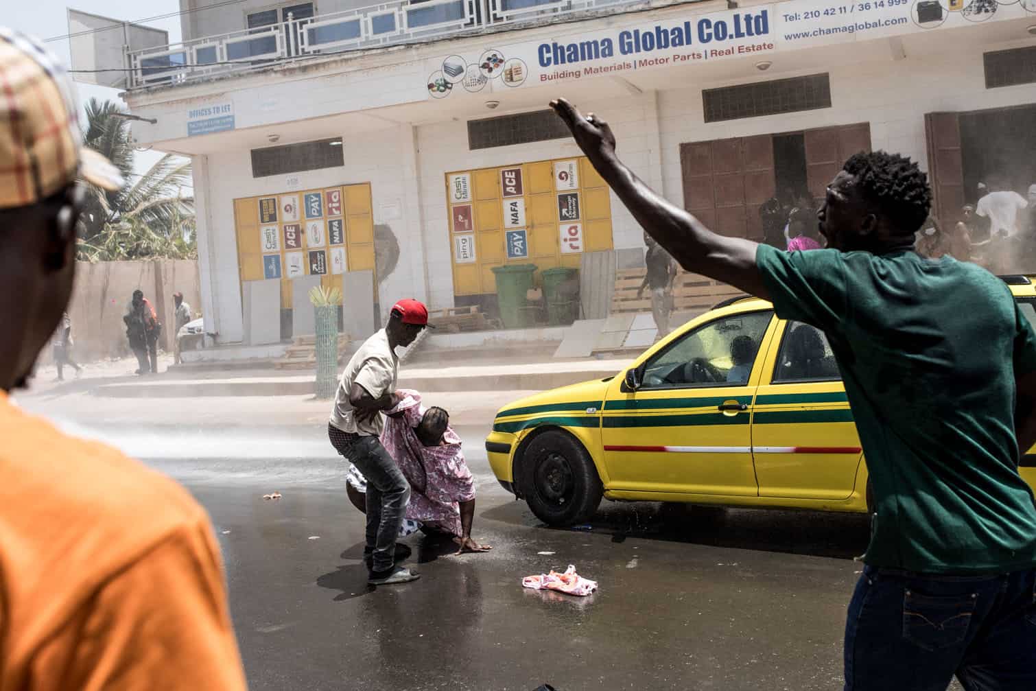 A man helps a woman as a Gambian Police water cannon sprays water