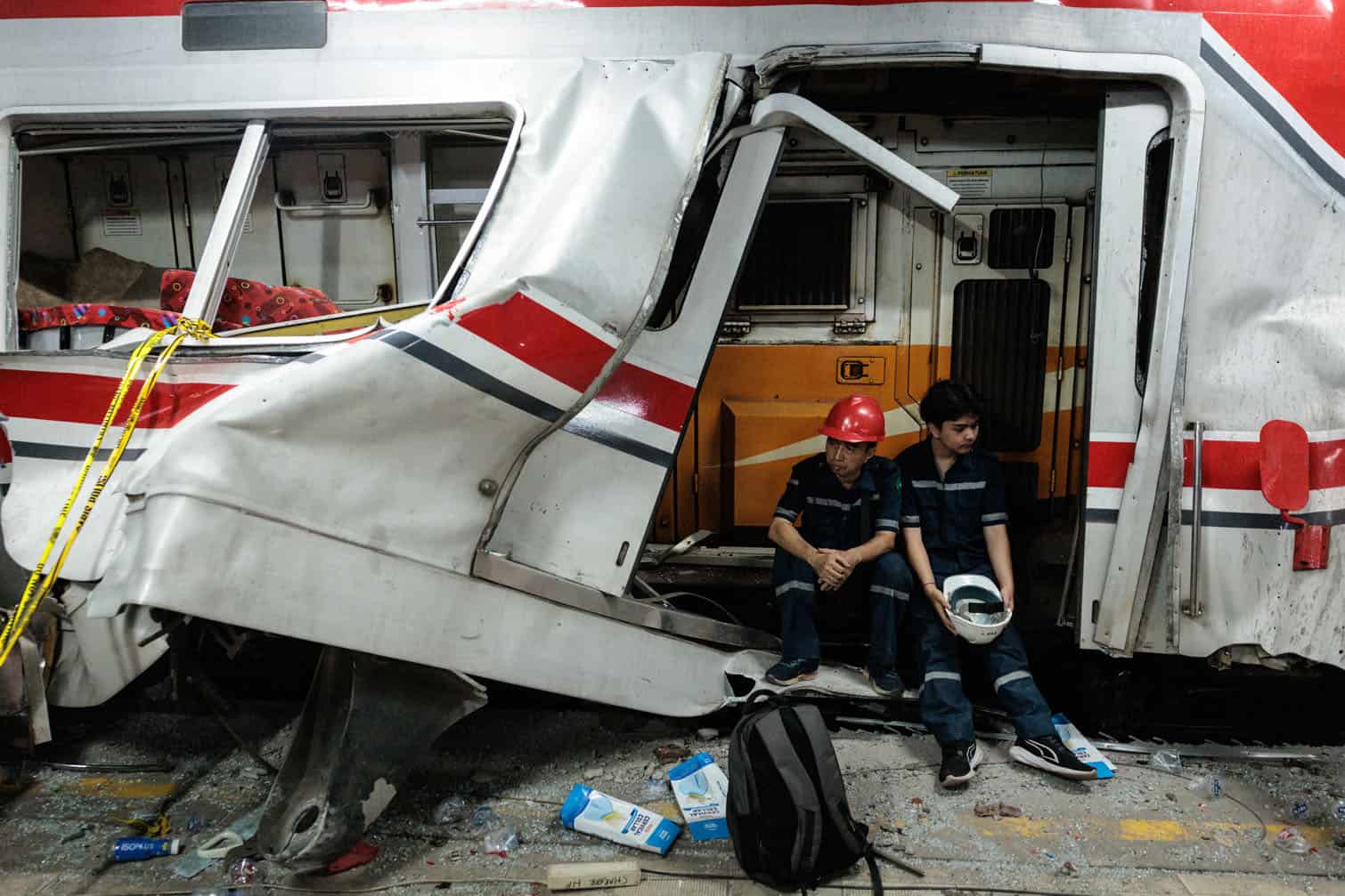 Workers sit at the site of a train collision