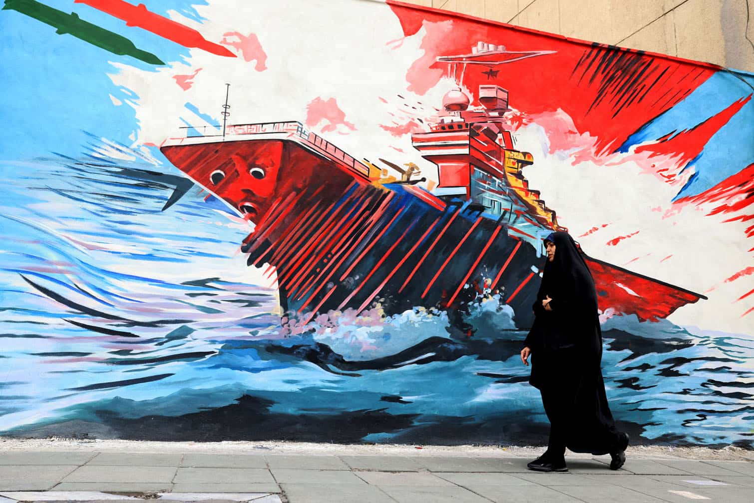 A woman walks past an anti-US and anti-Israel mural