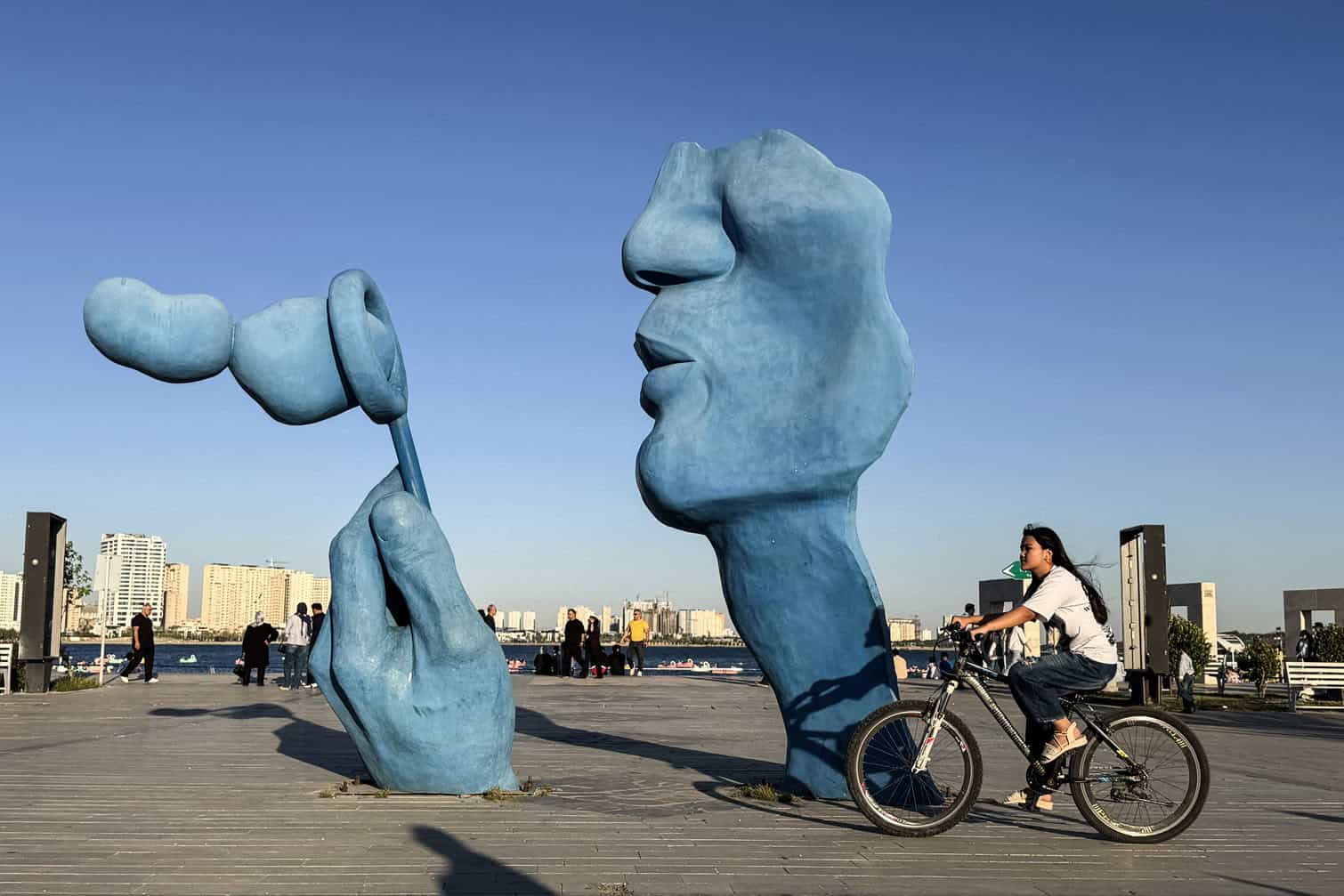A woman cycles past a sculpture at Chitgar Lake