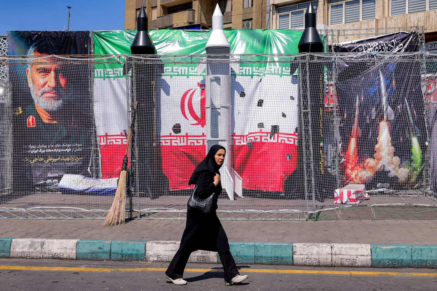 A woman walks past mockups of Iranian missiles
