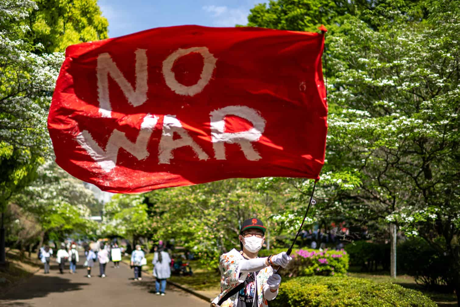 A demonstrator holds a flag reading "No War"