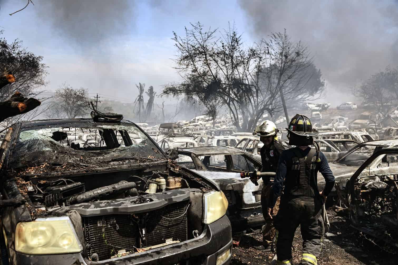 Firefighters work on a fire on a lot where impounded vehicles are stored