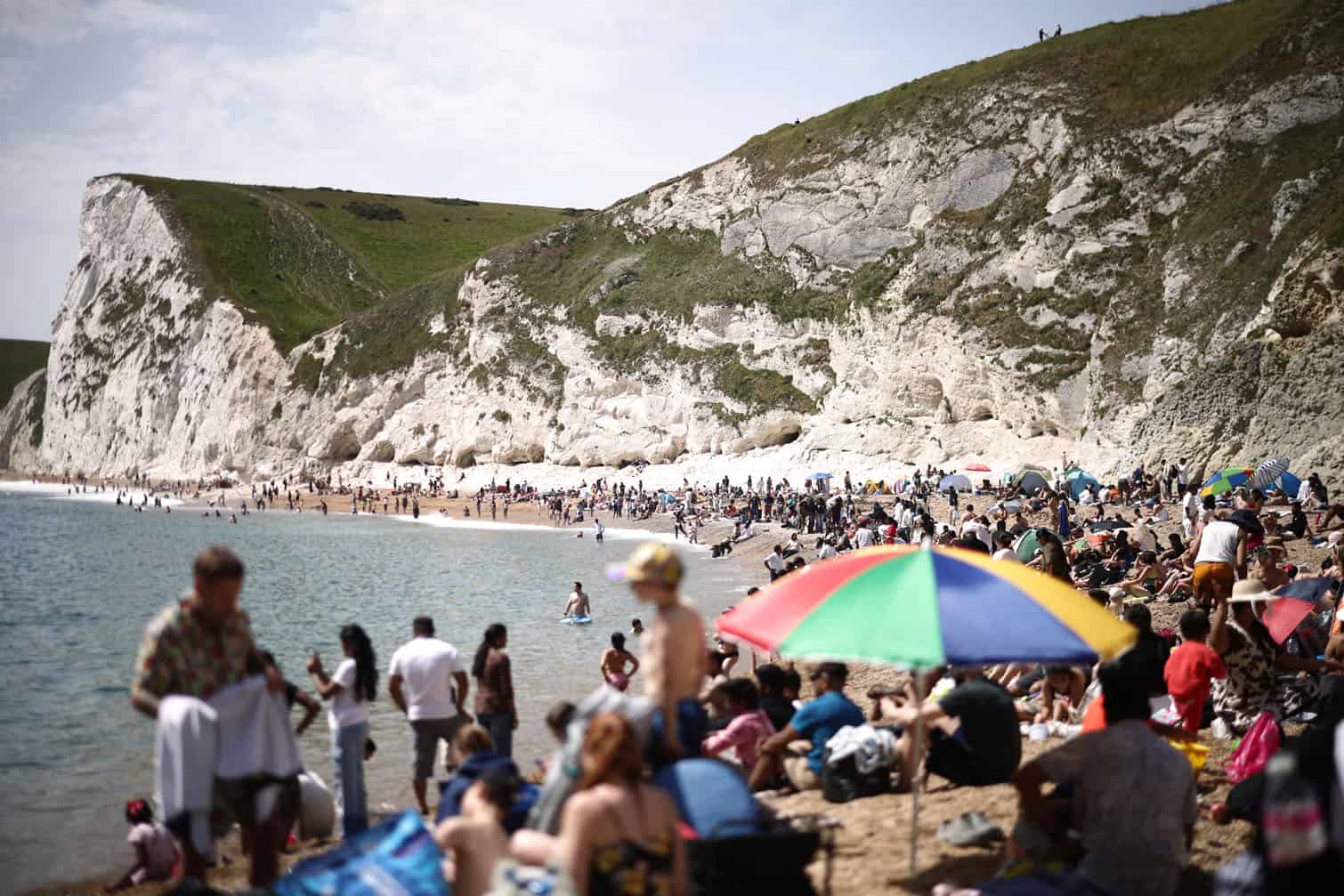People relax in the sunshine on Durdle Door beach