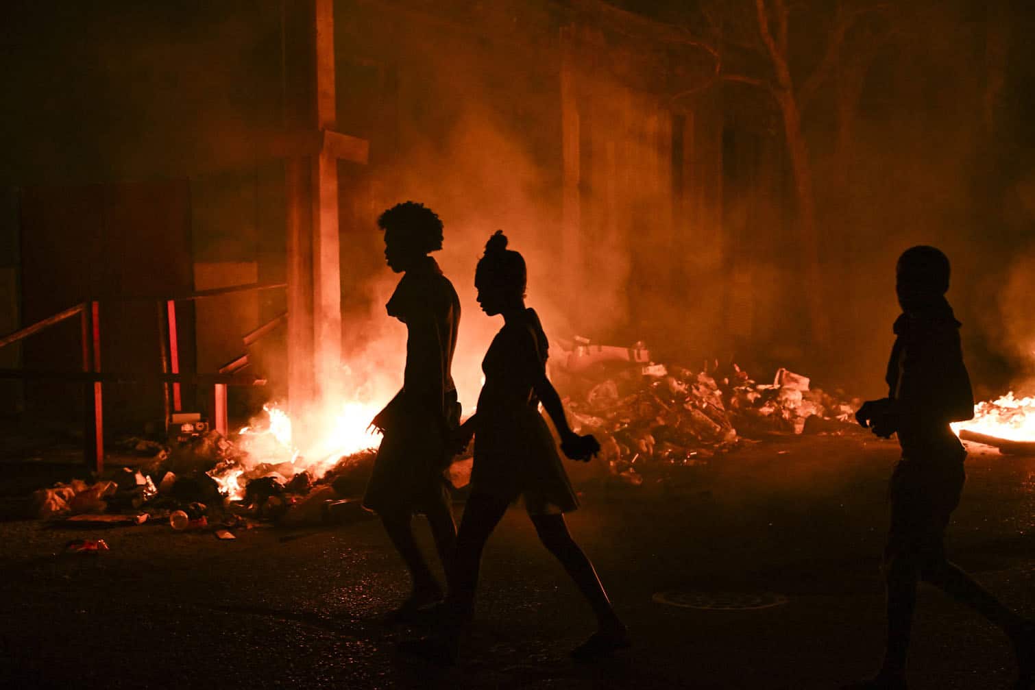 People walk past a fire set by demonstrators during a protest