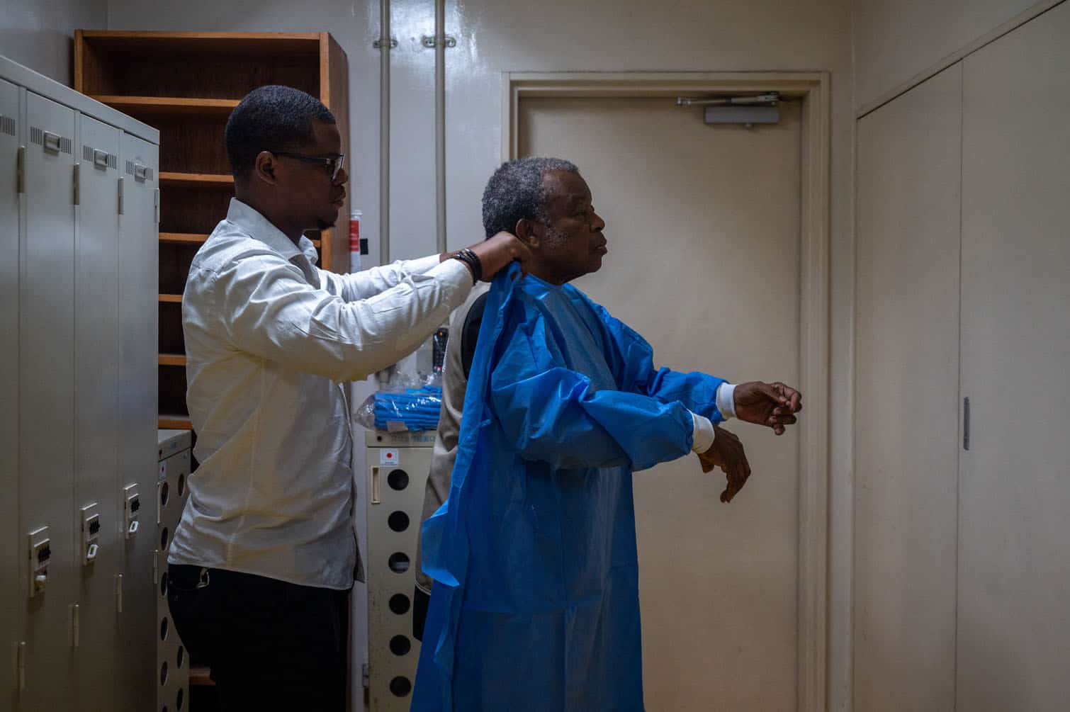 A worker (L) helps Professor Jean-Jacques Muyembe