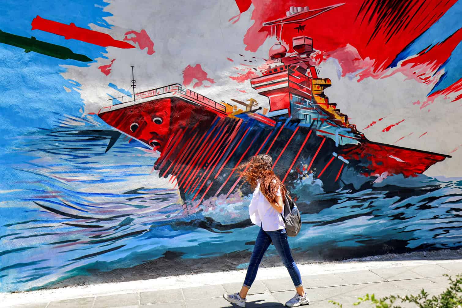 A woman walks past an anti-US and anti-Israel mural