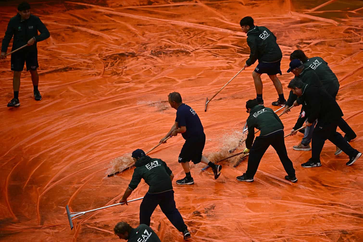 Staff remove water from the tarp covering the clay court