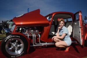 A pin up girl posing in front of a hotrod