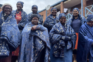 Elderly women wrapped in warm blue blankets during a winter community support drive.