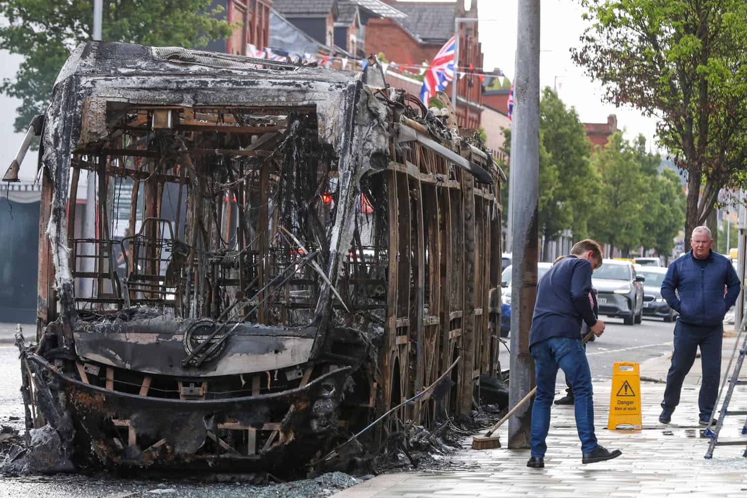 People clean the street next to a burnt-out "Glider city bus"